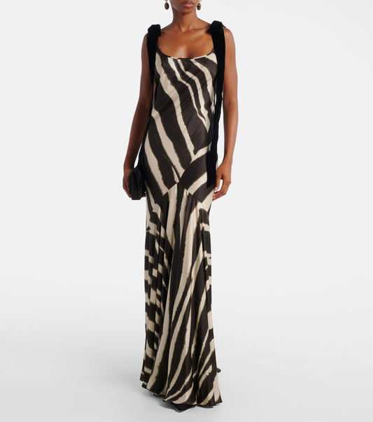 A woman modelling a floor-length, satin-look maxi dress featuring a bold, blurred zebra print and contrasting black textured shoulder ties.