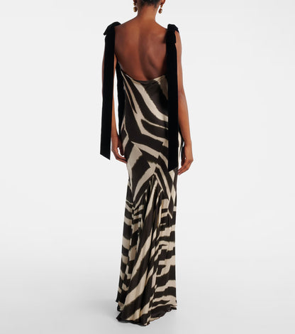 A woman modelling a floor-length, satin-look maxi dress featuring a bold, blurred zebra print and contrasting black textured shoulder ties.