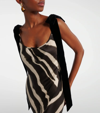A woman modelling a floor-length, satin-look maxi dress featuring a bold, blurred zebra print and contrasting black textured shoulder ties.