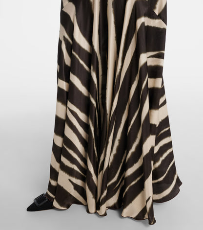 A woman modelling a floor-length, satin-look maxi dress featuring a bold, blurred zebra print and contrasting black textured shoulder ties.