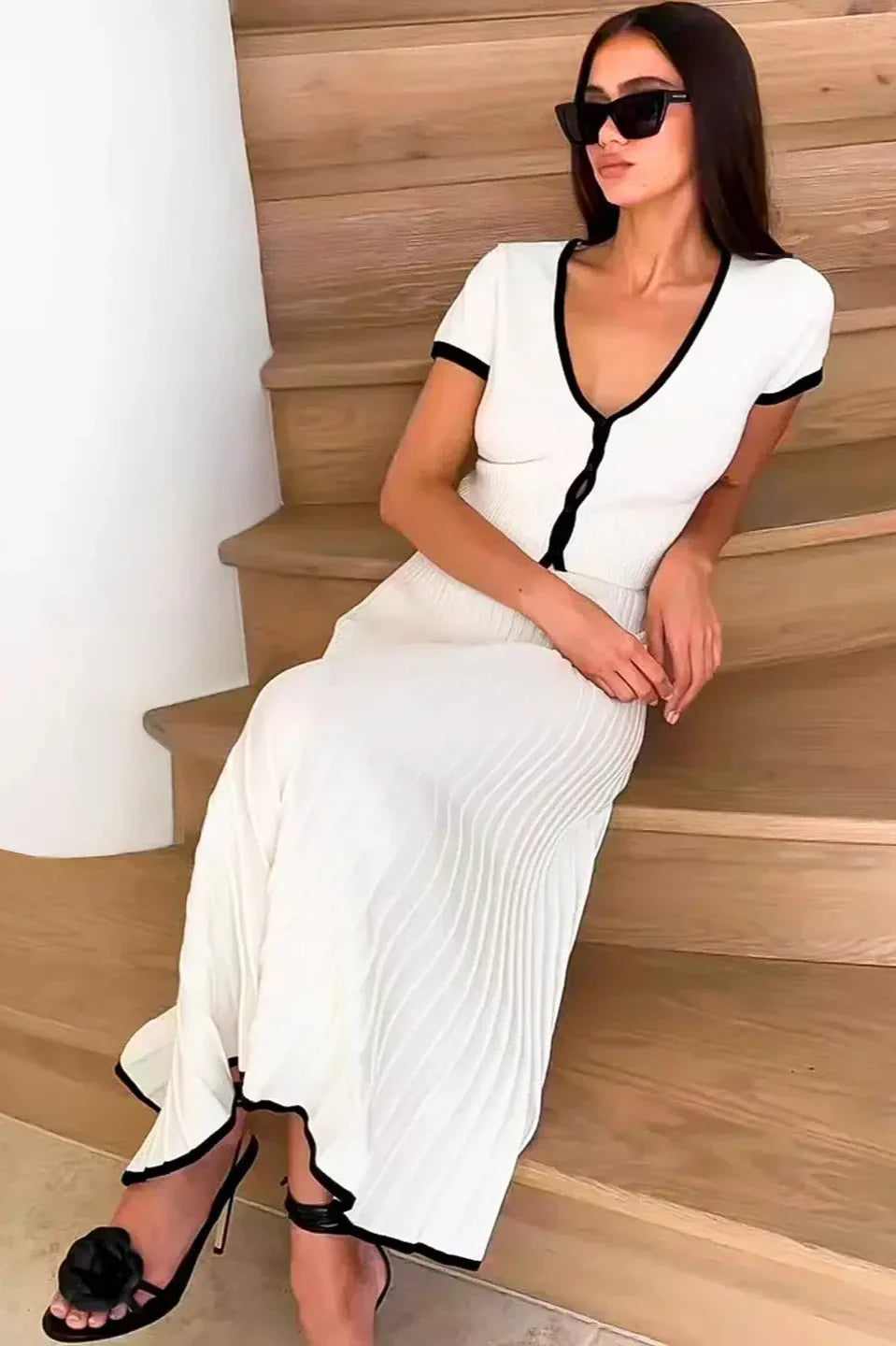 White - Woman wearing a white ribbed knit two-piece set featuring a short-sleeve V-neck crop top and a pleated midi skirt, both finished with black contrast trim.