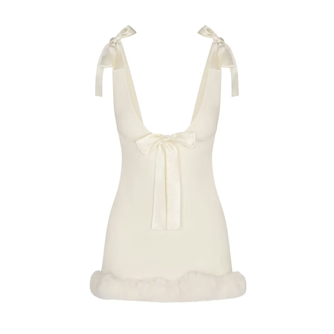 Ivory - A woman wearing a fitted white mini dress featuring a deep V-neckline, satin bow ties at the shoulders and bust, and a plush faux fur trim at the hem.