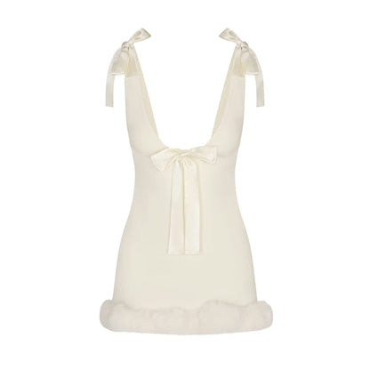 Ivory - A woman wearing a fitted white mini dress featuring a deep V-neckline, satin bow ties at the shoulders and bust, and a plush faux fur trim at the hem.
