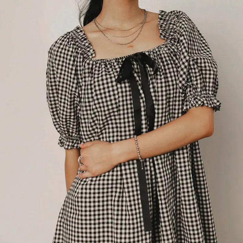 Black - Women's mini-length smock dress in a gingham print, featuring a square neckline with a ribbon tie and short puff sleeves.