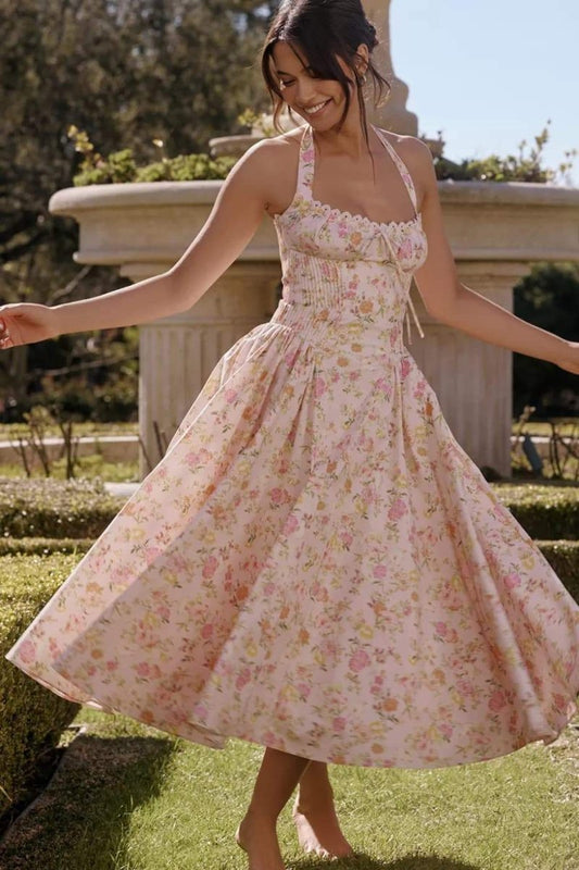 Pink - A woman twirling outdoors in a light pink midi dress featuring a vintage floral print, halter neckline, scalloped bust trim, ruched bodice, and a full flowing skirt.
