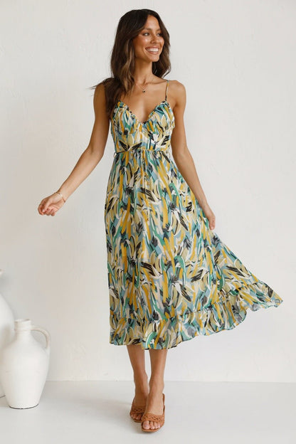 Yellow - A woman modelling a flowing midi dress featuring a vibrant abstract brushstroke print in yellow, green, and blue, complete with delicate straps and a ruffled hemline.