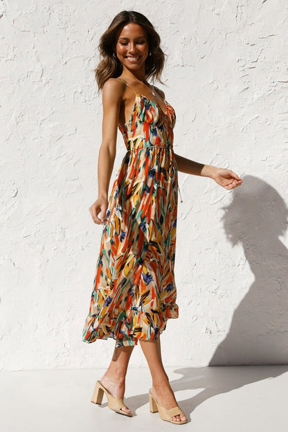 Red - A woman modelling a flowing midi dress featuring a vibrant abstract brushstroke print in yellow, green, and blue, complete with delicate straps and a ruffled hemline.