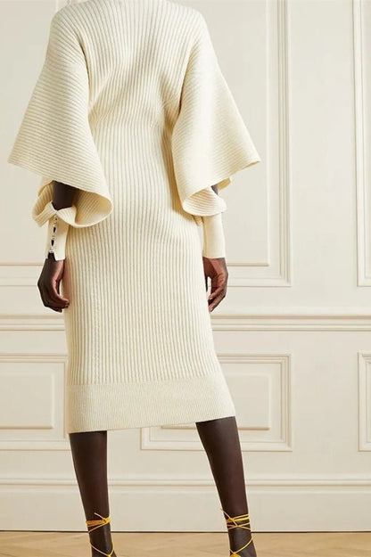White - A woman modeling a cream ribbed knit midi dress with a V-neckline and dramatic split fluted sleeves, holding a brown leather clutch.