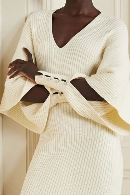 White - A woman modeling a cream ribbed knit midi dress with a V-neckline and dramatic split fluted sleeves, holding a brown leather clutch.