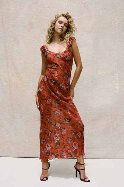 Red - A woman wearing a long, deep red maxi dress with a large pink rose floral print, featuring a scoop neckline and flutter cap sleeves.