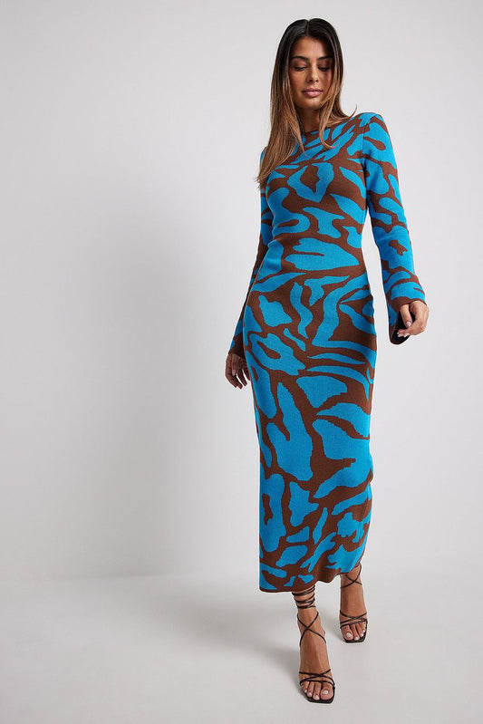Blue - A woman models a long-sleeve, crew neck maxi dress with a body-hugging fit. The knit dress features a bold abstract animal print in vibrant blue and rich brown. She is walking towards the camera against a plain white background.