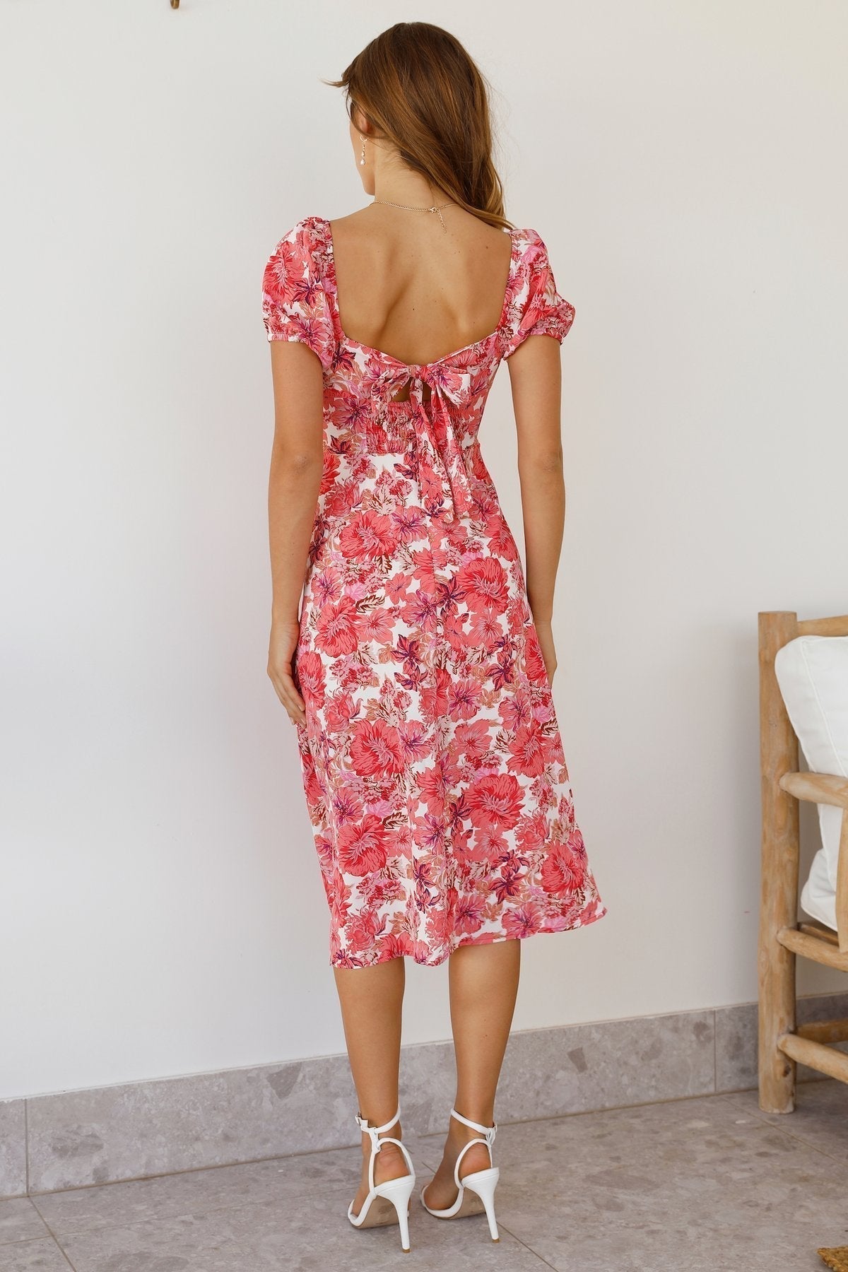 A woman wearing a vibrant pink and red floral midi dress with a sweetheart neckline, short puff sleeves, and a high side slit.