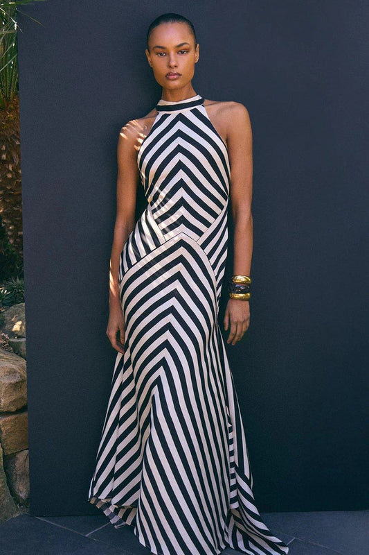 A woman models a sophisticated floor-length halter neck maxi dress featuring a bold, high-contrast geometric chevron stripe pattern.
