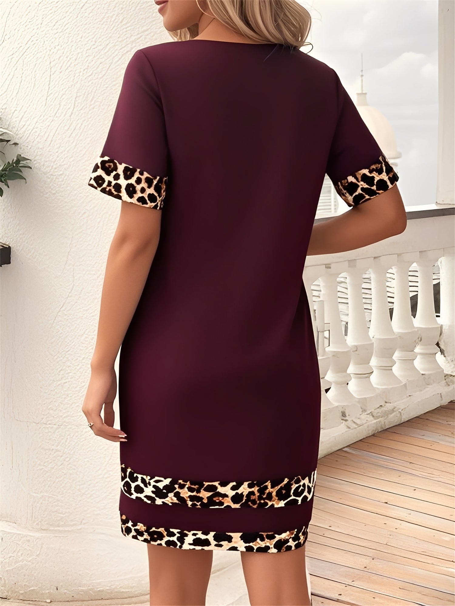Burgundy - Woman wearing a short-sleeve shift dress featuring a high crew neckline and contrasting leopard print trim on the sleeves and hem, standing on a balcony.