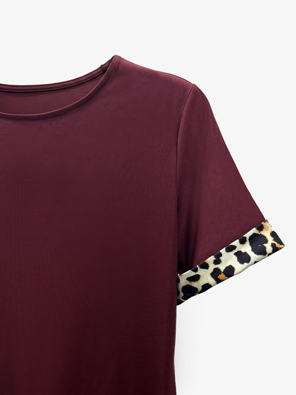 Burgundy - Woman wearing a short-sleeve shift dress featuring a high crew neckline and contrasting leopard print trim on the sleeves and hem, standing on a balcony.