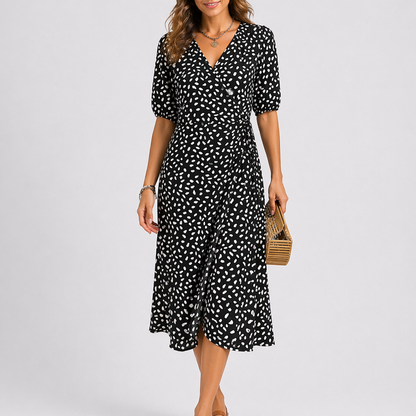 Black - Model wearing a speckled wrap midi dress with short sleeves and a side tie, styled with a woven clutch bag.