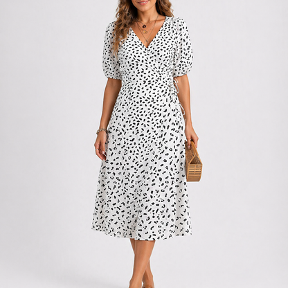 White - Model wearing a speckled wrap midi dress with short sleeves and a side tie, styled with a woven clutch bag.