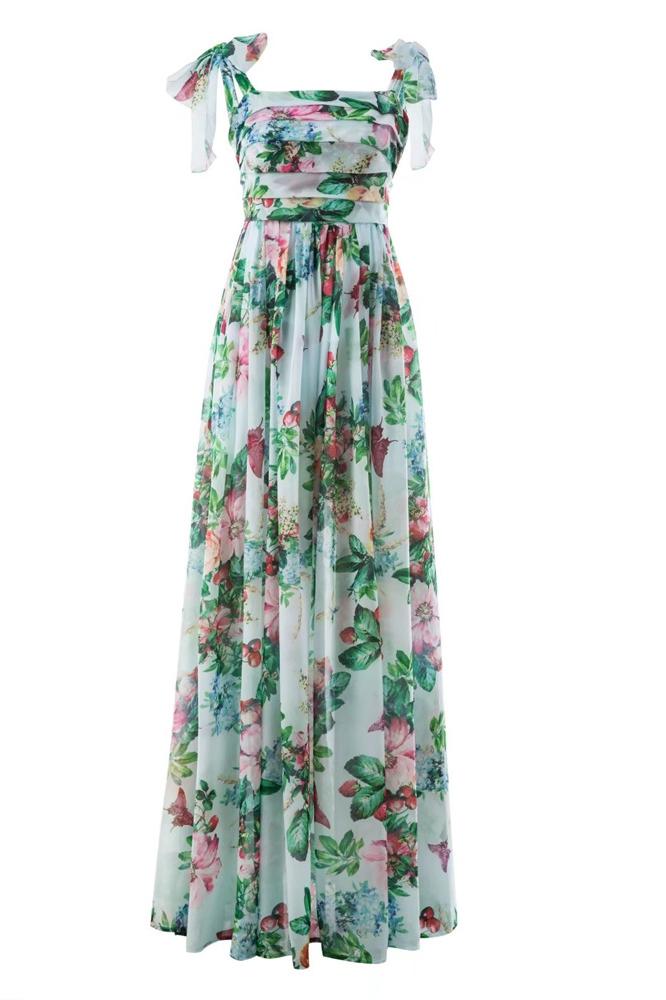Multi - A woman models a flowing maxi dress featuring a vibrant, large-scale botanical floral print, styled with a ruched bodice and wide tie-shoulder straps, standing outdoors near a floral arrangement.