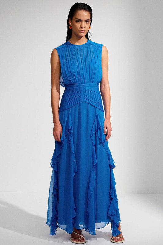 Blue - A woman models a vibrant blue sleeveless maxi dress featuring a finely pleated high-neck bodice, a wide ruched waistband, and a flowing sheer chiffon skirt with cascading vertical ruffles.