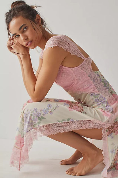 Pink - A woman wearing a maxi dress featuring a black lace bodice with an under-bust cut-out and a sheer skirt with a vibrant floral print and lace trim.