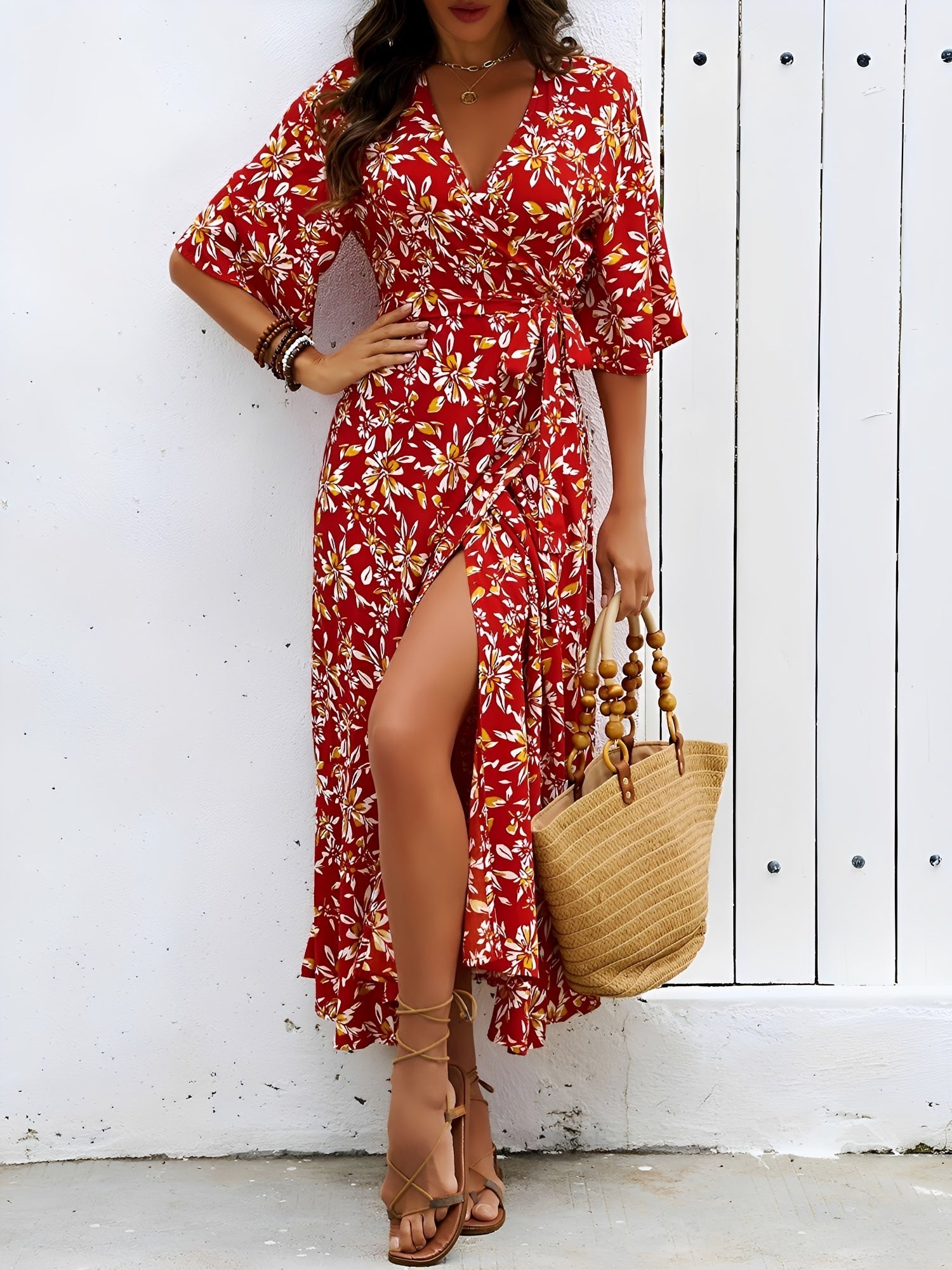 Red - Model wearing a floral V-neck wrap maxi dress with short sleeves and a waist tie, styled with a woven tote bag and sandals.