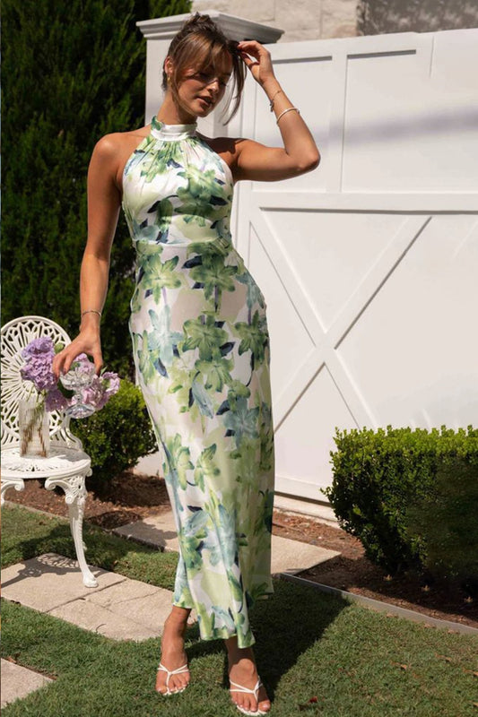 Green - A woman standing outdoors wearing an elegant, high halter neck maxi dress with a smooth satin finish and a large-scale green botanical floral print.