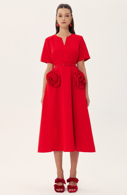 Red - A woman wearing a bright red, short-sleeved midi dress featuring a notched V-neckline, a thin waist belt, and two large 3D rosette embellishments on the A-line skirt.