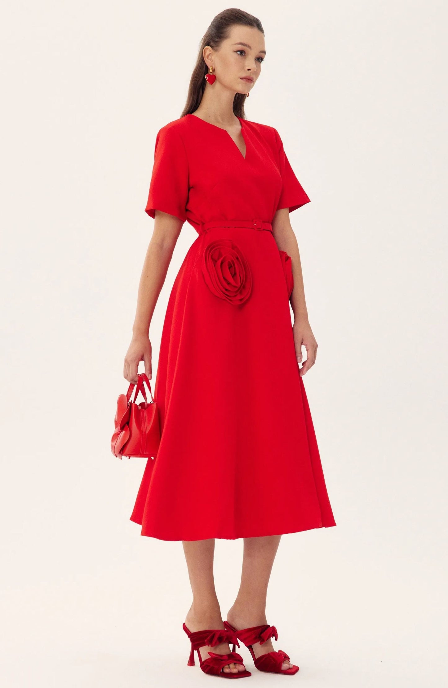 Red - A woman wearing a bright red, short-sleeved midi dress featuring a notched V-neckline, a thin waist belt, and two large 3D rosette embellishments on the A-line skirt.