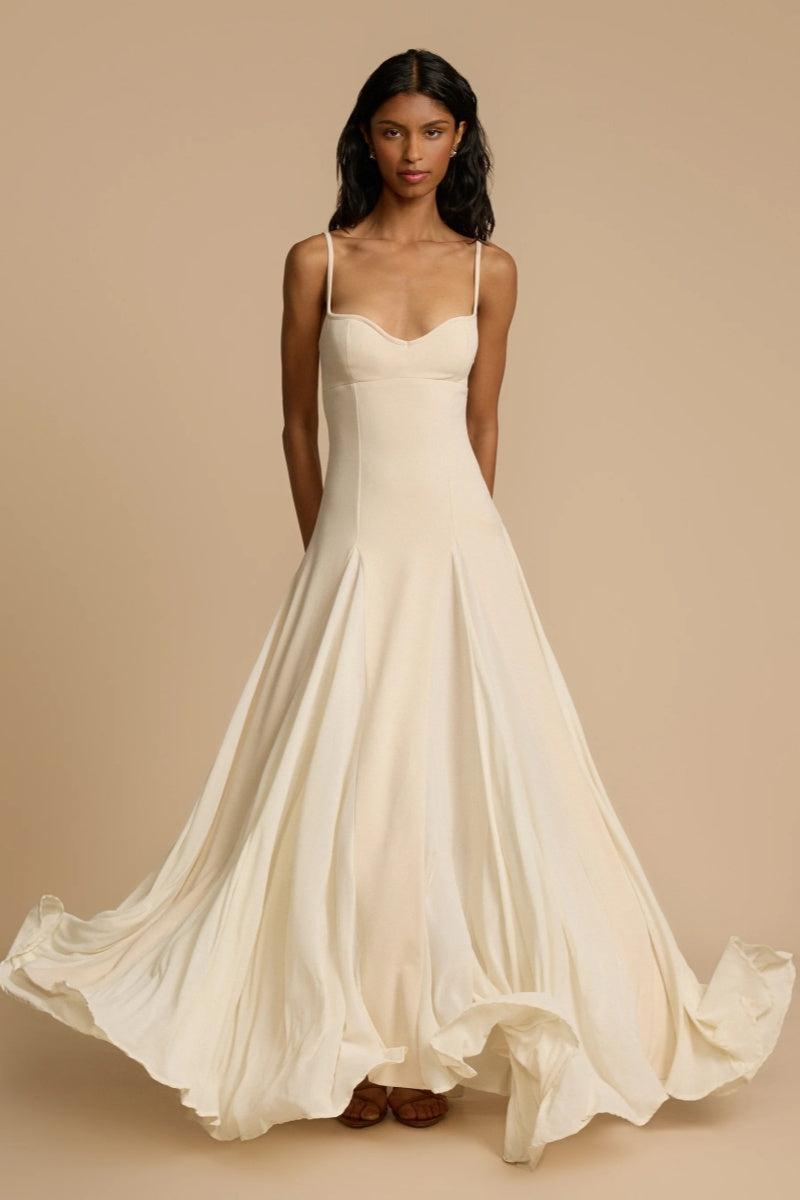 Ivory - A woman wearing a long, cream-coloured maxi dress with a sweetheart neckline, slim straps, and a voluminous skirt with godet pleats.