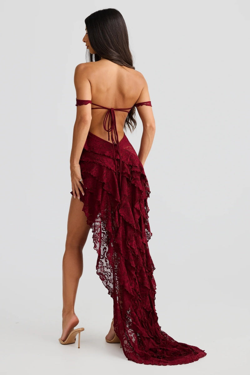 Red - A woman wearing a dark red, off-the-shoulder maxi dress made of floral lace, featuring a ruched bodice, a high front slit with cascading ruffles, and a dramatic back train.