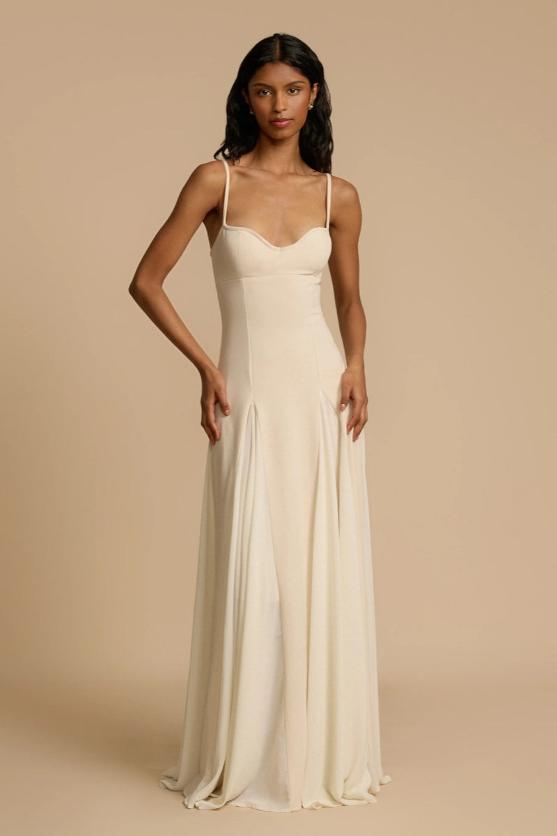 Ivory - A woman wearing a long, cream-coloured maxi dress with a sweetheart neckline, slim straps, and a voluminous skirt with godet pleats.