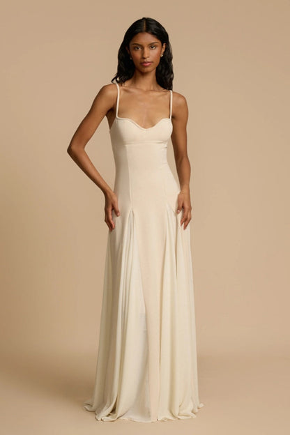 Ivory - A woman wearing a long, cream-coloured maxi dress with a sweetheart neckline, slim straps, and a voluminous skirt with godet pleats.