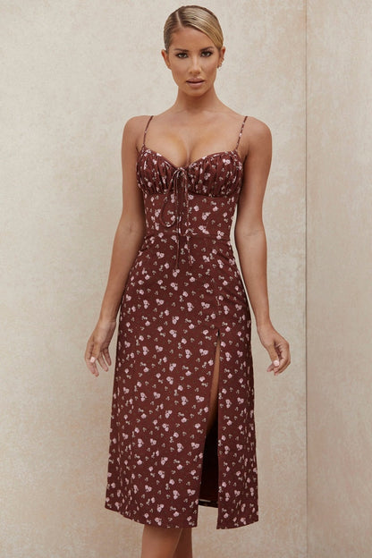 Women's brown midi dress featuring a ditsy floral print, ruched bust with tie detail, spaghetti straps, and a high thigh slit.
