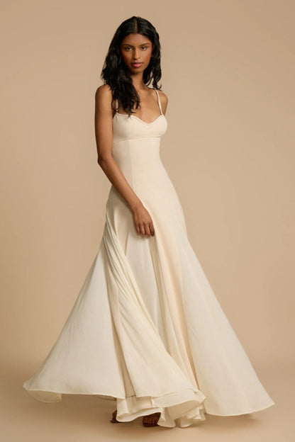 Ivory - A woman wearing a long, cream-coloured maxi dress with a sweetheart neckline, slim straps, and a voluminous skirt with godet pleats.
