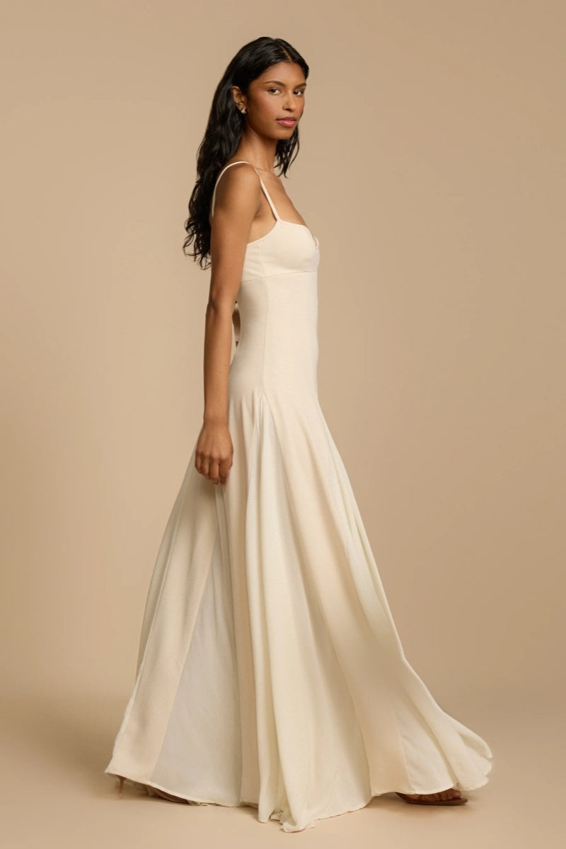 Ivory - A woman wearing a long, cream-coloured maxi dress with a sweetheart neckline, slim straps, and a voluminous skirt with godet pleats.