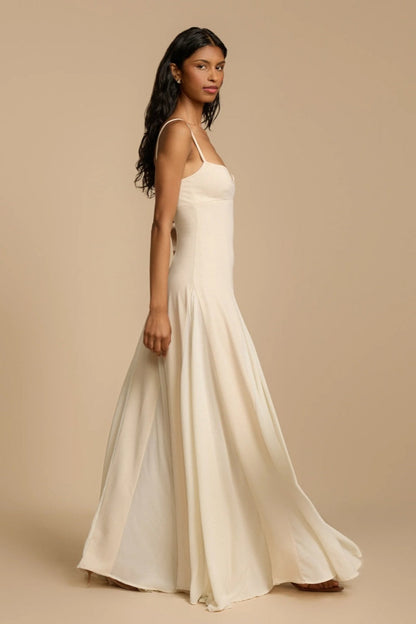 Ivory - A woman wearing a long, cream-coloured maxi dress with a sweetheart neckline, slim straps, and a voluminous skirt with godet pleats.