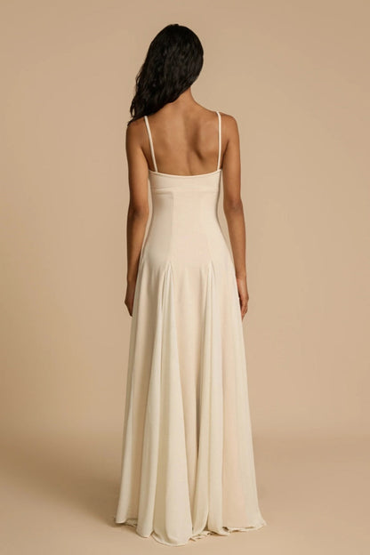 Ivory - A woman wearing a long, cream-coloured maxi dress with a sweetheart neckline, slim straps, and a voluminous skirt with godet pleats.