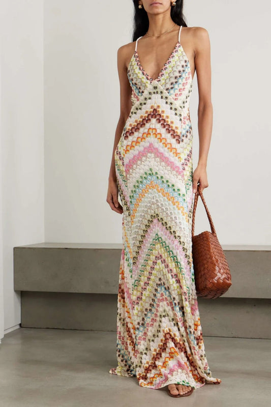Multicolor - A woman wearing a floor-length, multi-coloured chevron print plissé maxi dress with a plunging V-neckline and spaghetti straps, holding a brown woven leather bag.