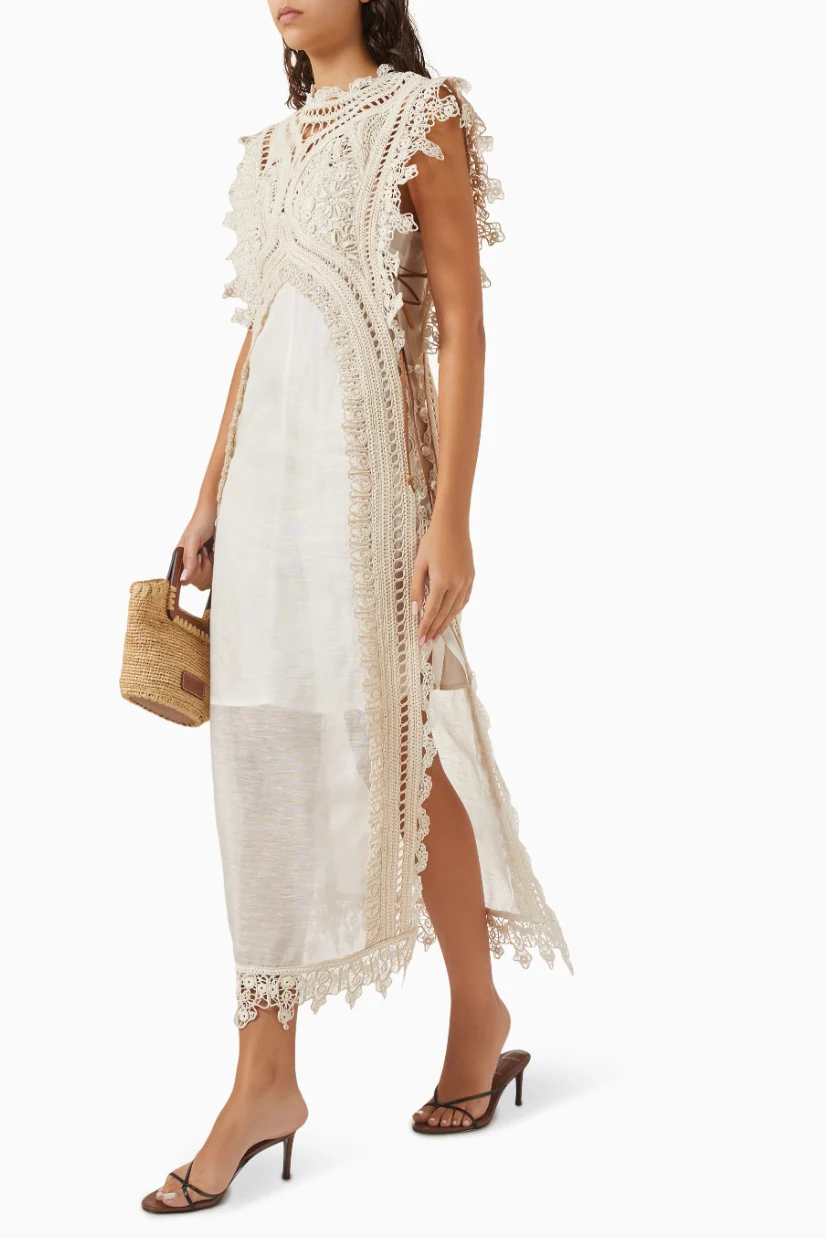 A woman wearing a cream-coloured midi dress featuring an intricate crochet overlay with scalloped edges over a semi-sheer slip.