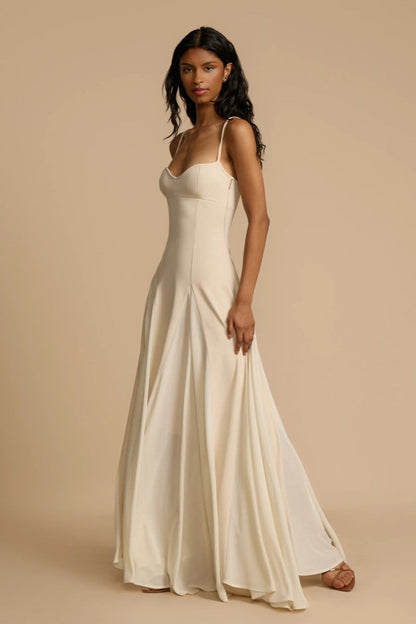 Ivory - A woman wearing a long, cream-coloured maxi dress with a sweetheart neckline, slim straps, and a voluminous skirt with godet pleats.