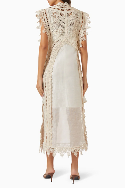 A woman wearing a cream-coloured midi dress featuring an intricate crochet overlay with scalloped edges over a semi-sheer slip.