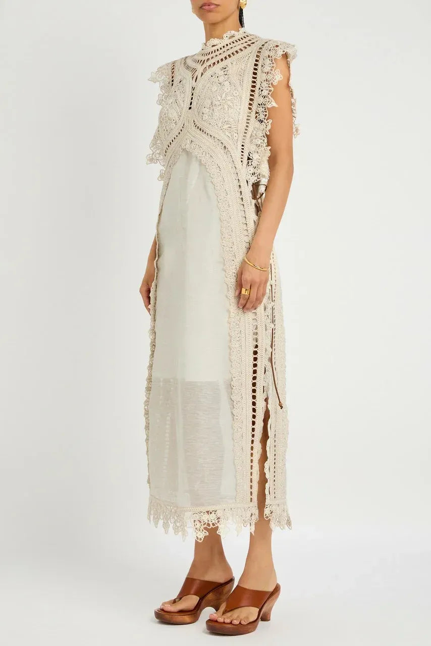 Apricot - A woman wearing a cream-coloured midi dress featuring an intricate crochet overlay with scalloped edges over a semi-sheer slip.