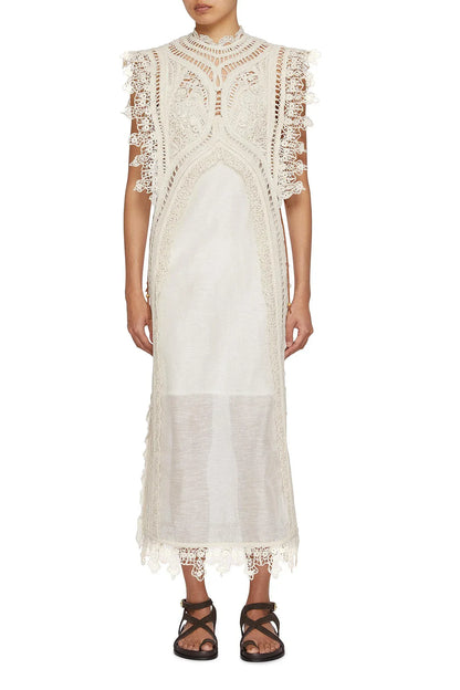 Apricot - A woman wearing a cream-coloured midi dress featuring an intricate crochet overlay with scalloped edges over a semi-sheer slip.