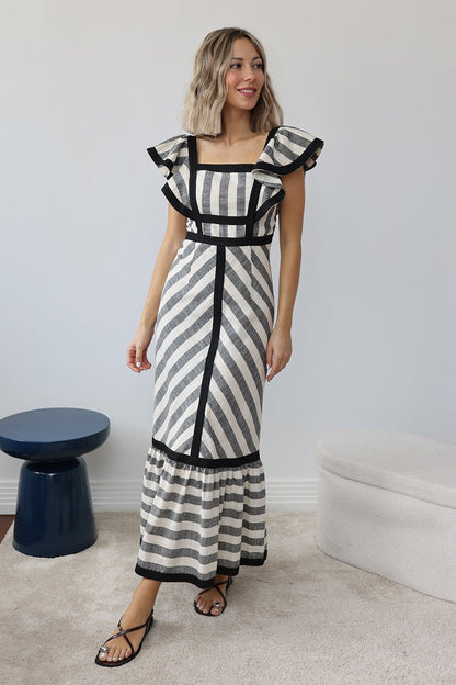 Stripe - A woman wearing a structured maxi dress with a square neckline, ruffled shoulders, and a tiered hem, featuring a bold mixed-direction stripe pattern and contrast black binding.