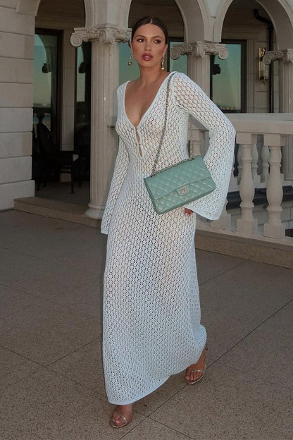 White - A woman wearing a white, semi-sheer crochet maxi dress with long flared sleeves and a deep V-neckline with keyhole detailing, standing outdoors.