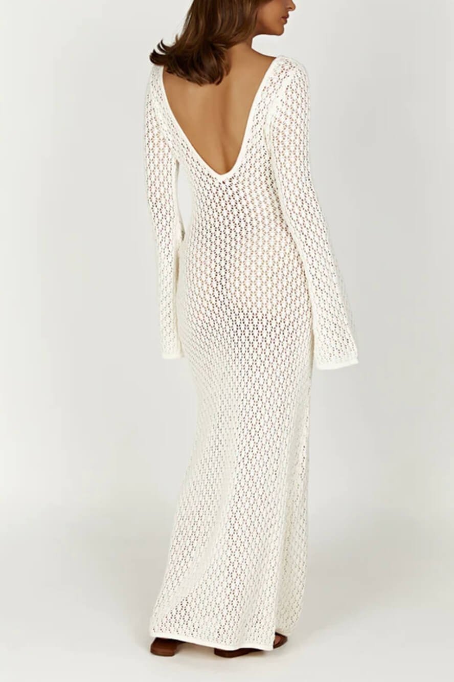White - A woman wearing a white, semi-sheer crochet maxi dress with long flared sleeves and a deep V-neckline with keyhole detailing, standing outdoors.