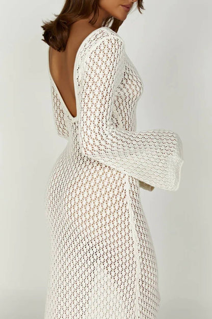 White - A woman wearing a white, semi-sheer crochet maxi dress with long flared sleeves and a deep V-neckline with keyhole detailing, standing outdoors.
