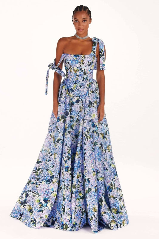 Blue - A woman models an elegant floor-length maxi dress featuring a structured corset bodice, tie-shoulder straps, and a vibrant blue and green floral print on a crisp, voluminous fabric.