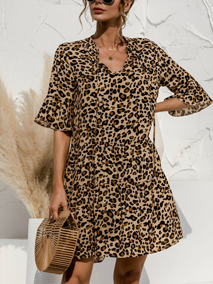 Leopard - Model wearing a woven leopard print v-neck tiered mini dress with flutter sleeves and neckline tie details, holding a structured bamboo handbag.