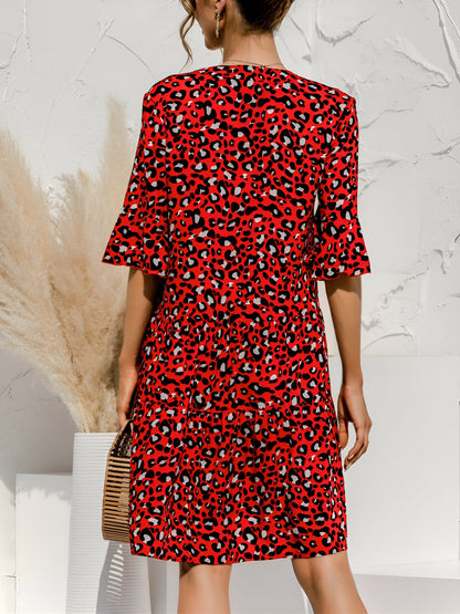 Red - Model wearing a woven leopard print v-neck tiered mini dress with flutter sleeves and neckline tie details, holding a structured bamboo handbag.